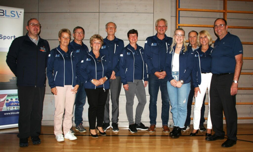 Gruppe Menschen stehen in einer Turnhalle vor einem BLSV-Aufsteller in Jacken mit BLSV und BSJ Logos