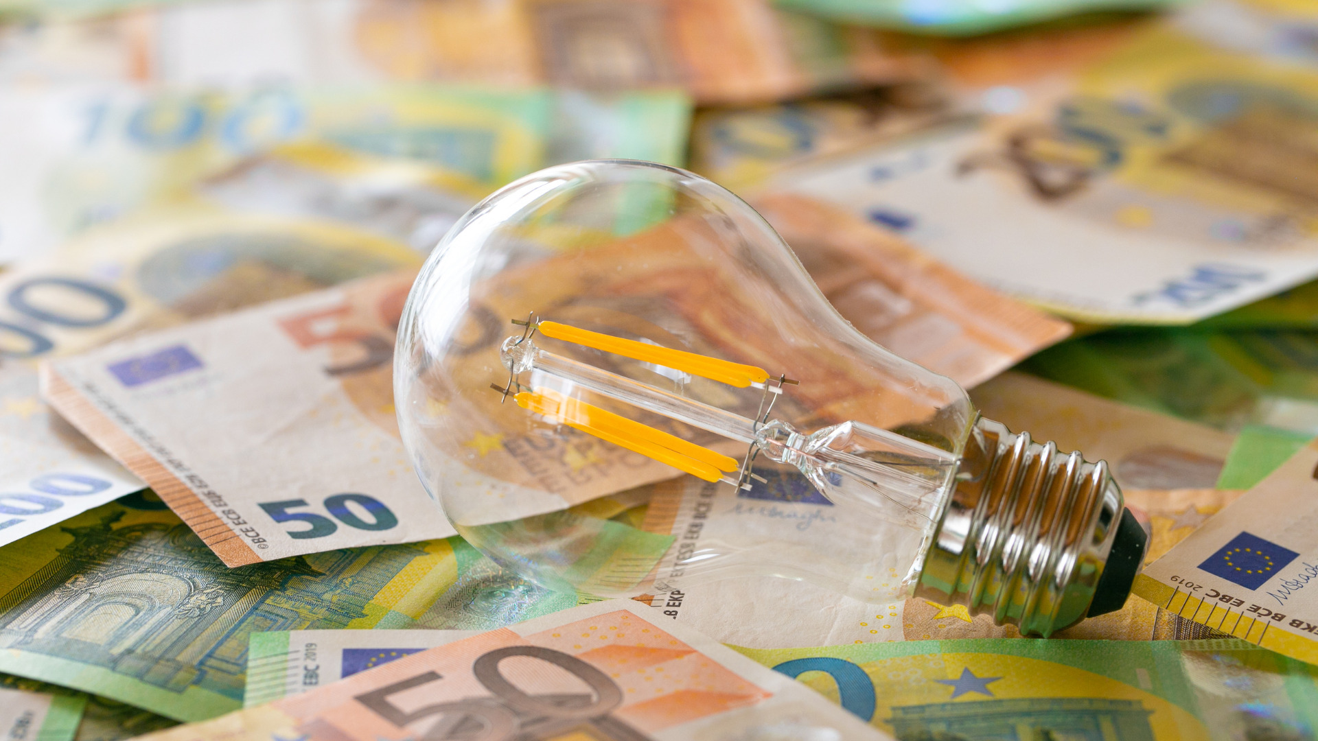 Eine Glühbirne liegt auf einer Fläche von ausgelegten Euro-Noten verschiedener Höhe