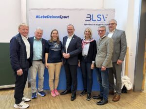 Eine Gruppe Menschen stehen vor einer aufegbauten Wand mit dem BLSV Logo